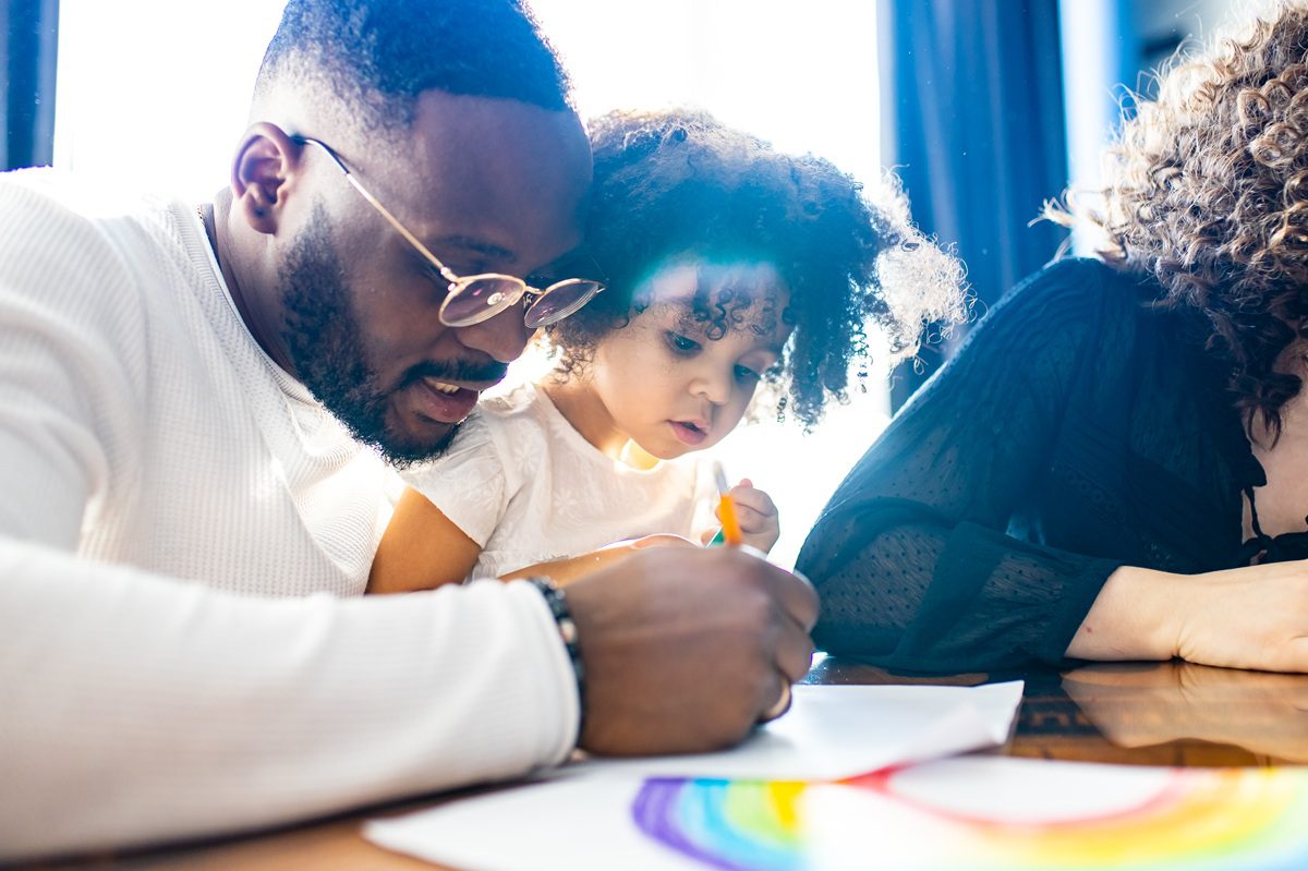 father wearing glasses and adorable little daughter drawing colorful pencils spending leisure time on weekend together.